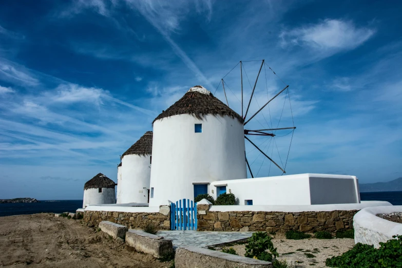 a white house with two windmills next to the ocean