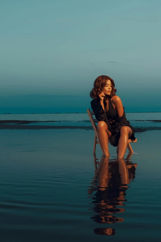 a woman in a dark bathing suit sits on a chair near the ocean