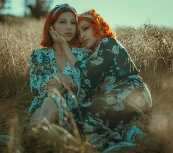 two girls sit in a field hugging each other