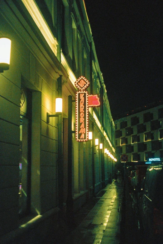 there is a dark street in the city that has a neon sign on it