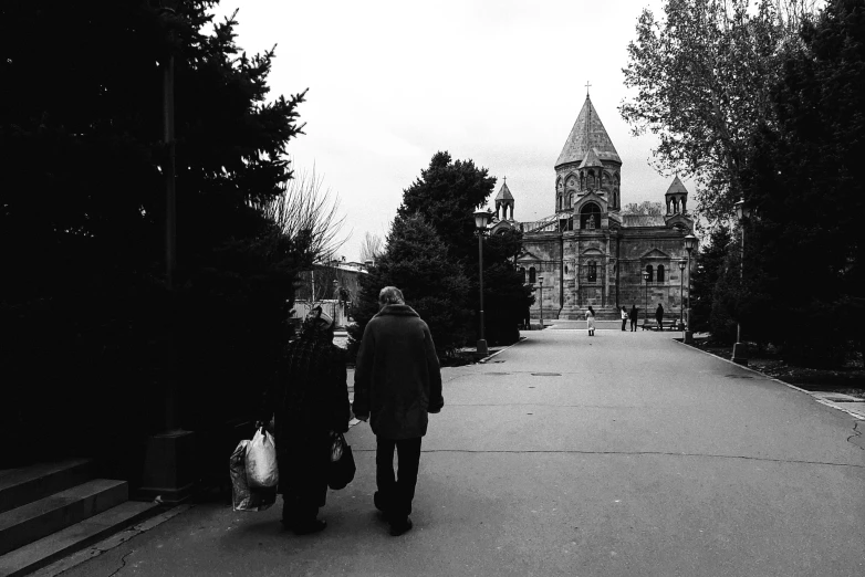 two people walking down the sidewalk towards a building