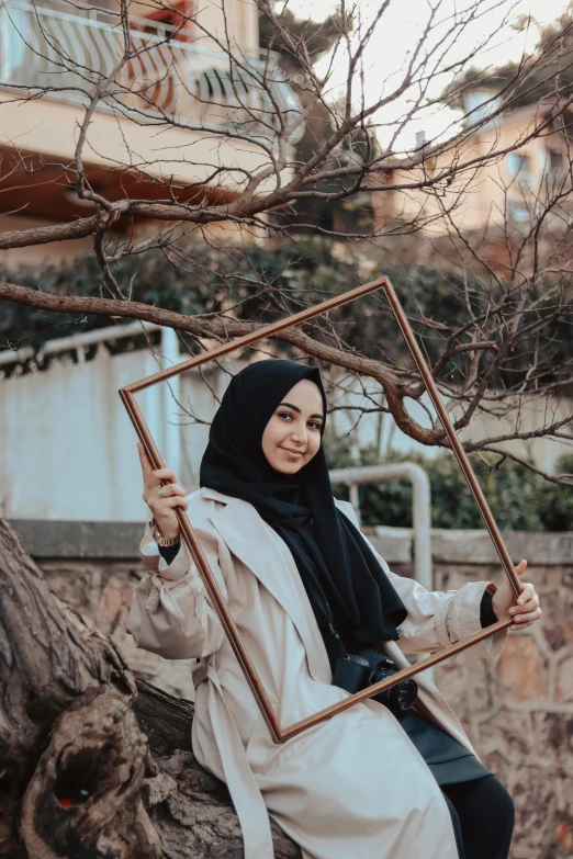 a woman wearing a hijab sitting on a tree nch in front of a mirror