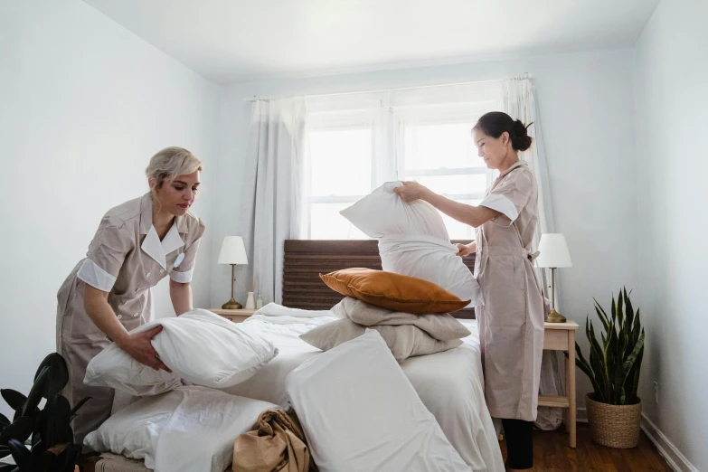 two women standing near bed with pillows on top of them