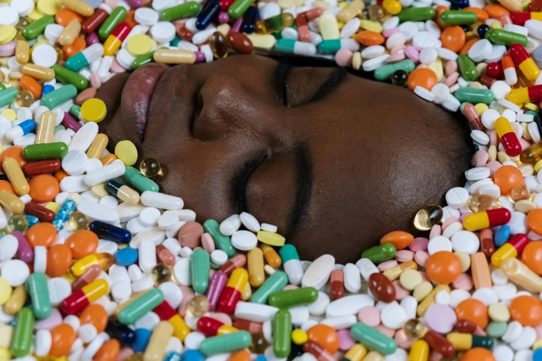 a dark skinned person sleeping among the multi - colored pills, medicine and pills