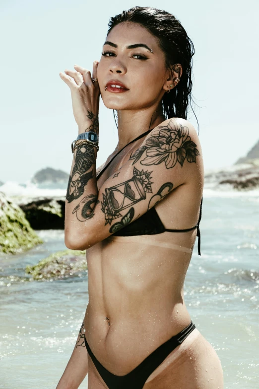 a woman with tattoos stands by the ocean