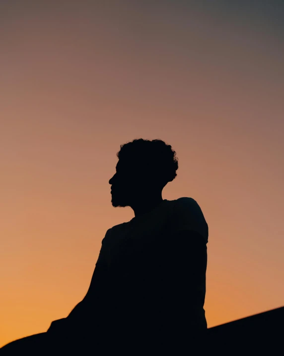 a man looks into the distance in front of an orange sunset