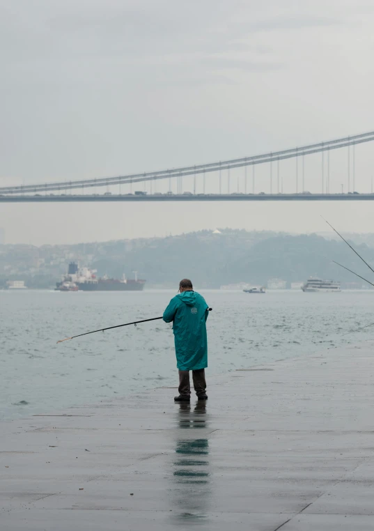 the man is fishing on the water near a bridge