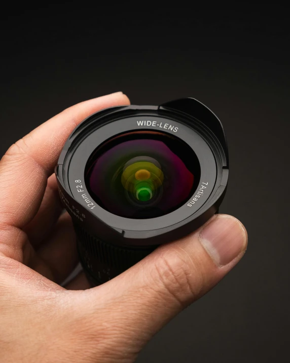 hand holding up small camera lens against a dark background