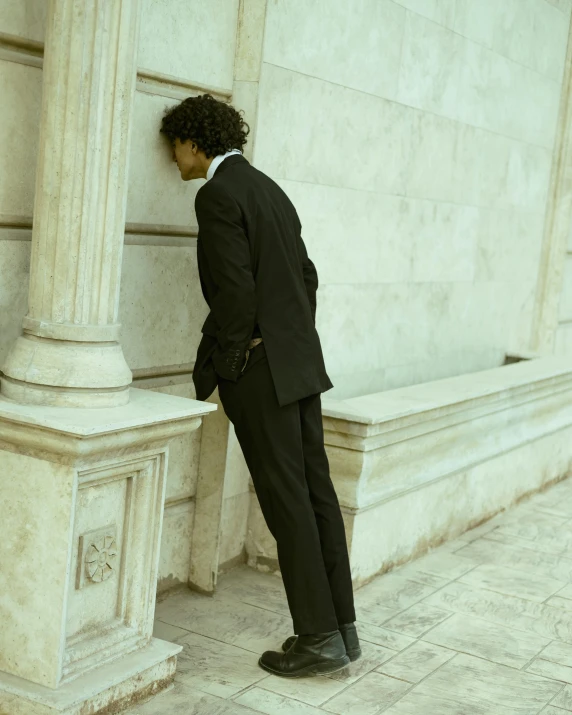 a man wearing a suit leaning against a wall