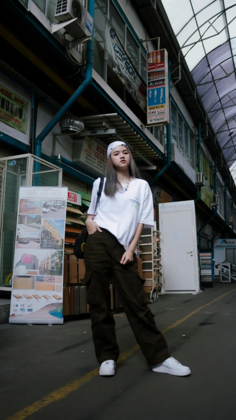 a woman wearing brown pants and a white t - shirt in a warehouse