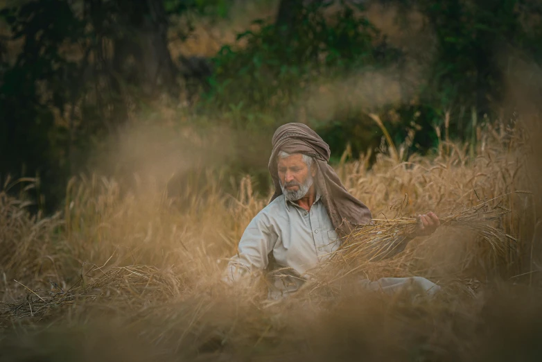 an older man with a turban is sitting in the grass
