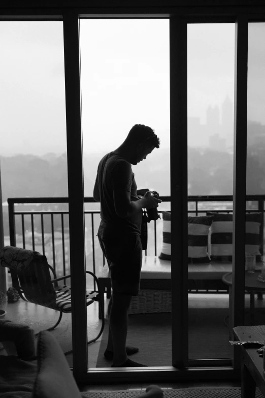 man looking at cell phone in front of large window