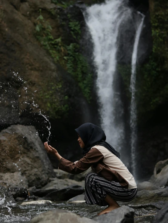 an image of a person crouching on the rocks with water coming from the waterfall