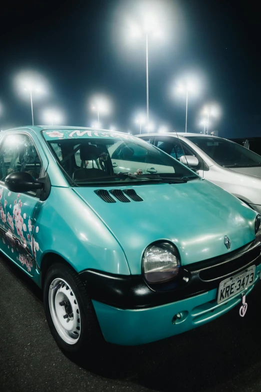 a small blue vehicle is parked in a parking lot with lights