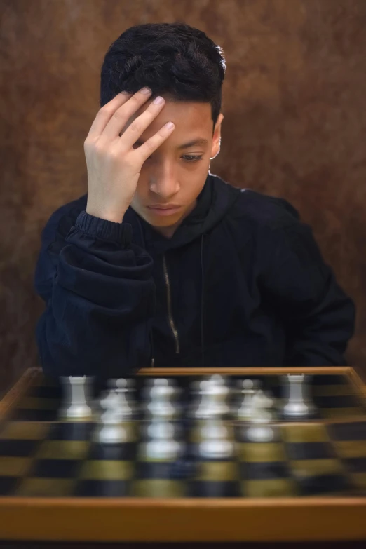 a man looking at chess pieces while sitting at a table