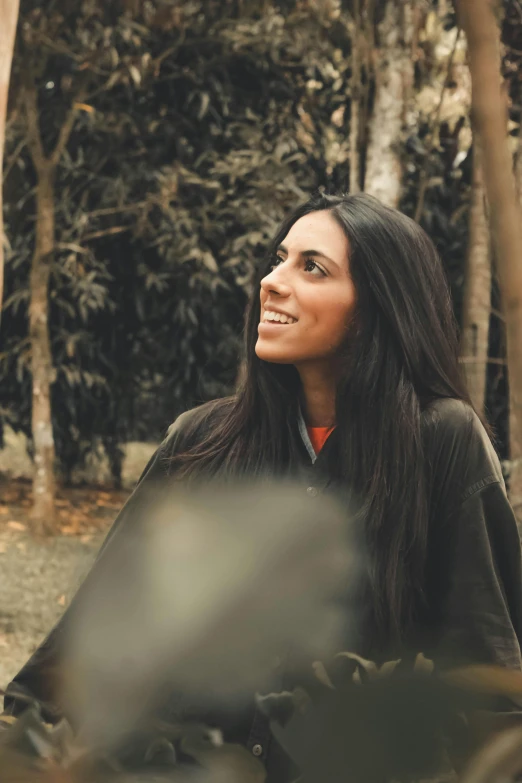 a smiling woman sitting in the woods and looking up