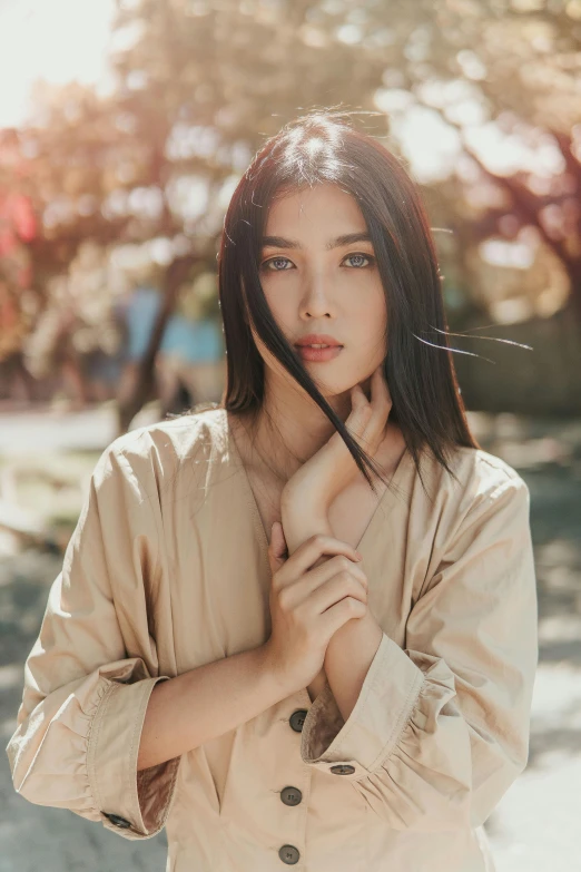 young woman in beige trenchcoat leaning against tree