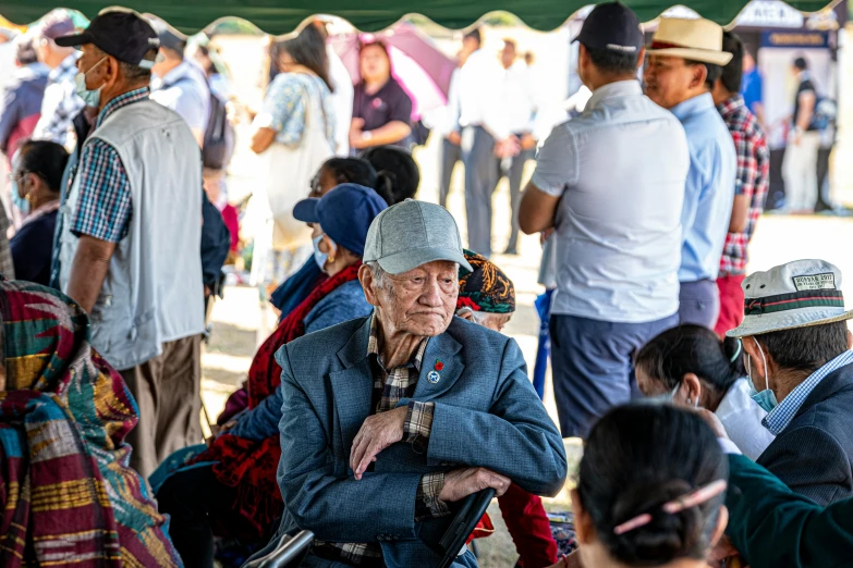 an old man sitting in a chair in the middle of a crowded area