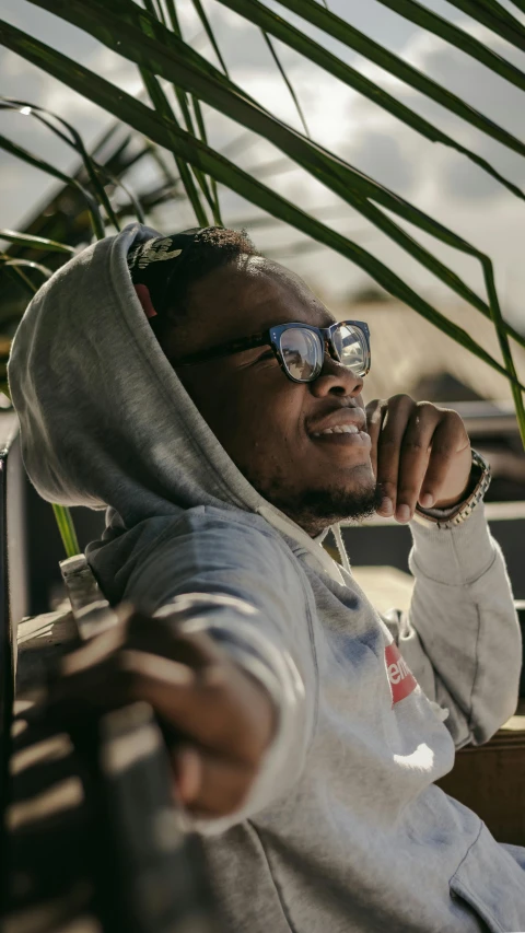 a man with sunglasses and a hoodie on sits down