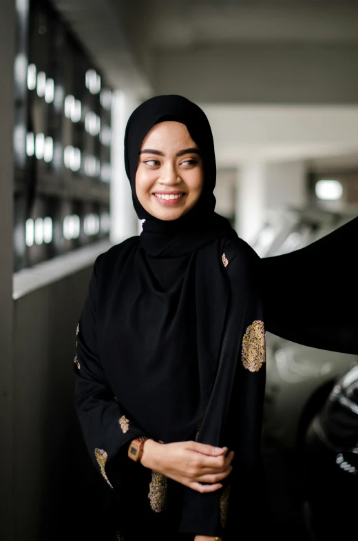 a woman wearing a black hijab smiling and standing