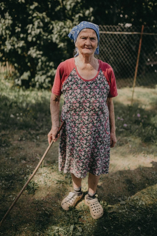 old woman standing in front of some bushes wearing a blue head covering