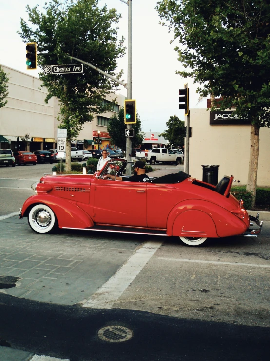 a red old time car on the road at an intersection