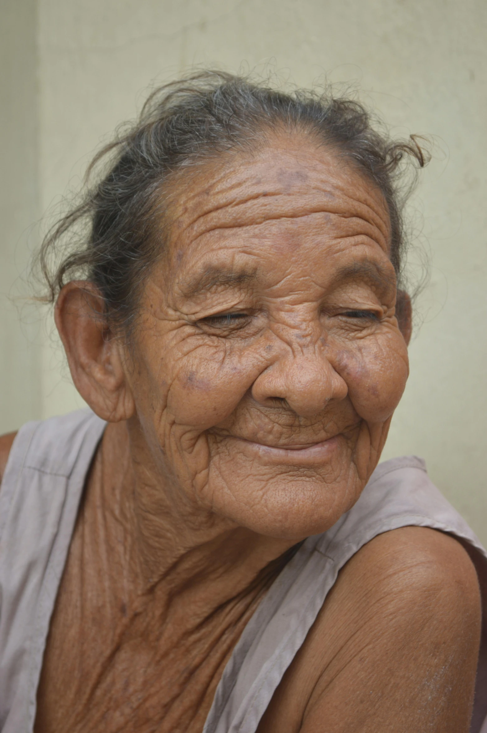 an old woman in a grey top smiles with wrinkles on her face