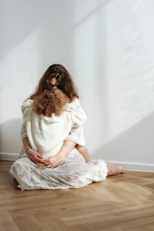 a girl sitting on the floor with long hair wearing a white knitted dress