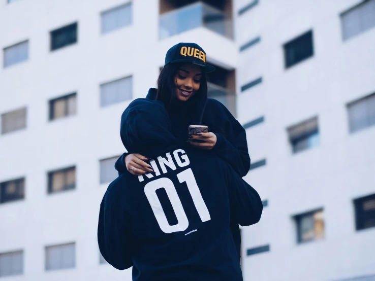 an attractive young woman with black hair, wearing a hoodie, texting on her phone and holding a bag