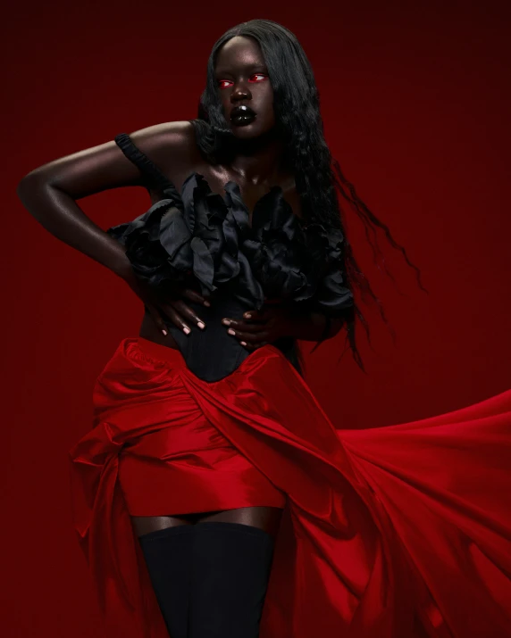 a woman standing against a red wall with her arms on her hips