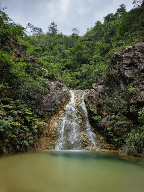 a small waterfall in the middle of a rocky hill next to a body of water