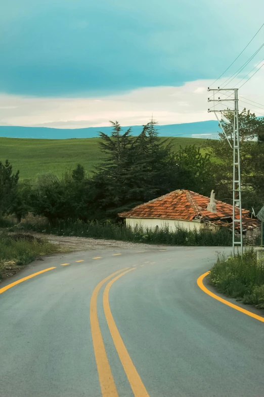 a road curves away from a red roofed barn