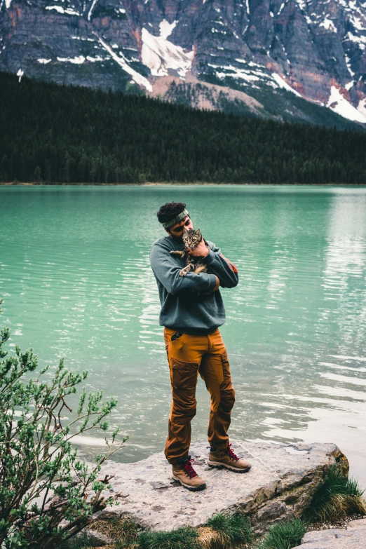 a man with his hands over his face on a mountain ledge looking at the water