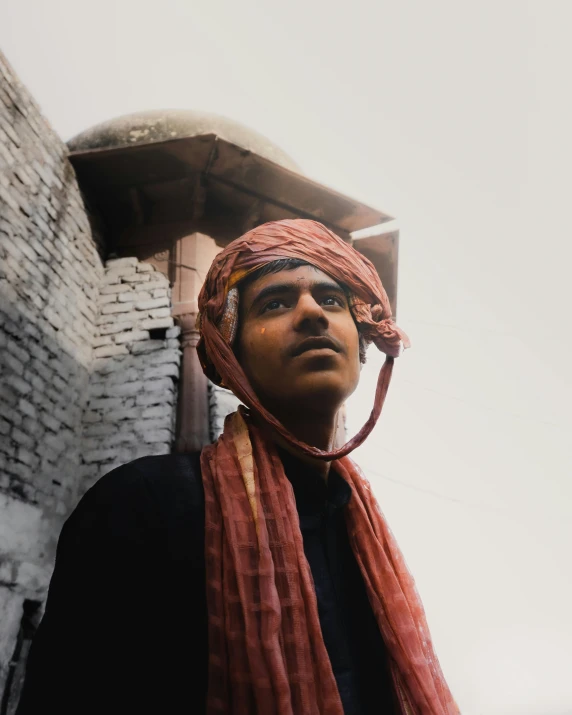 a man wearing a red scarf and head wrap standing against a building