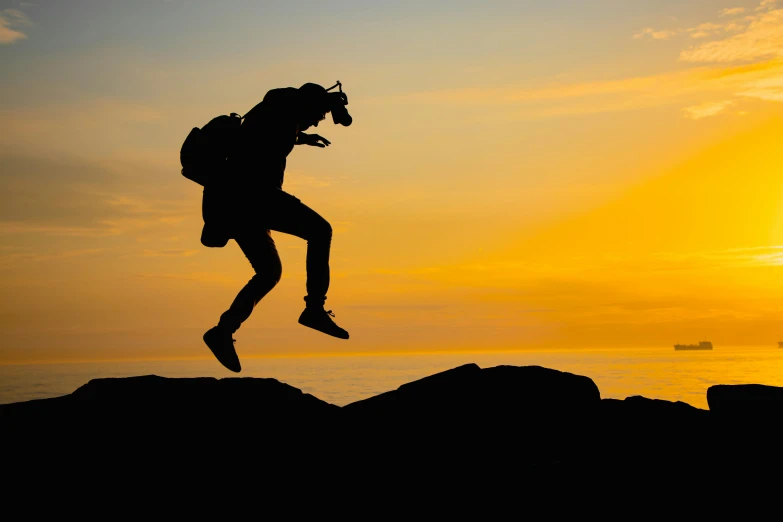 the silhouette of a man jumping off rocks into the water