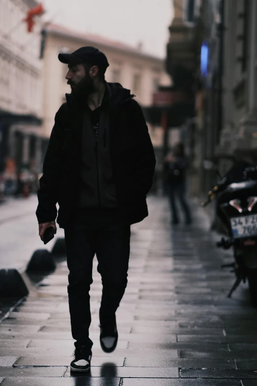 a man walks down a wet, city sidewalk