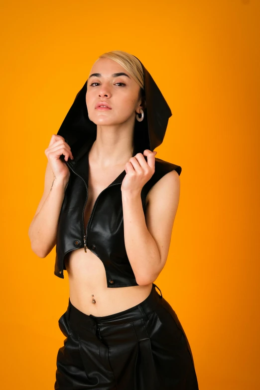 woman posing wearing black leather outfit in front of a yellow backdrop