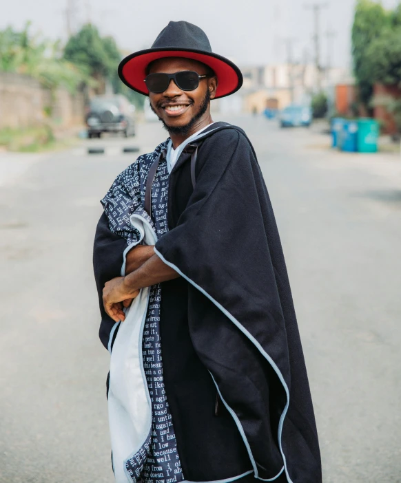 a man wearing a hat and sunglasses standing on the side of the street