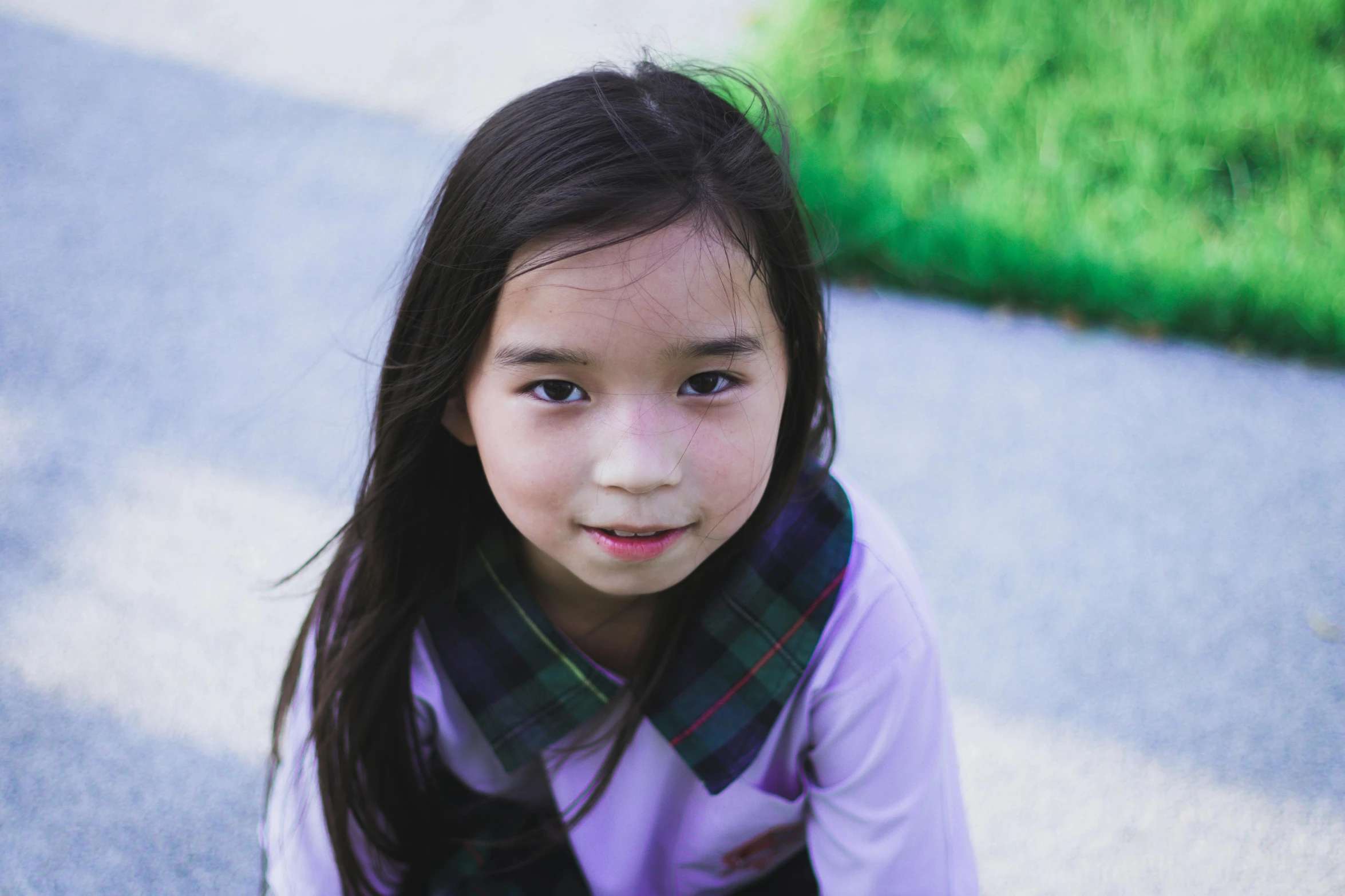 a little girl with long hair is sitting in the middle of a park