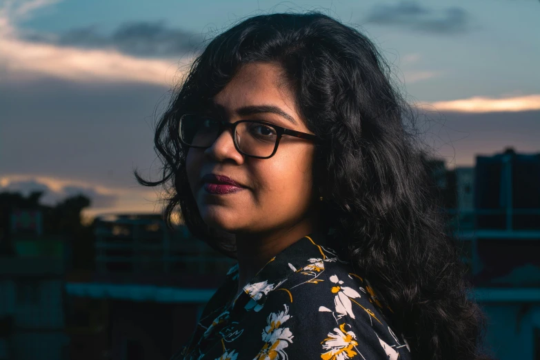 a woman with glasses looking ahead at sunset