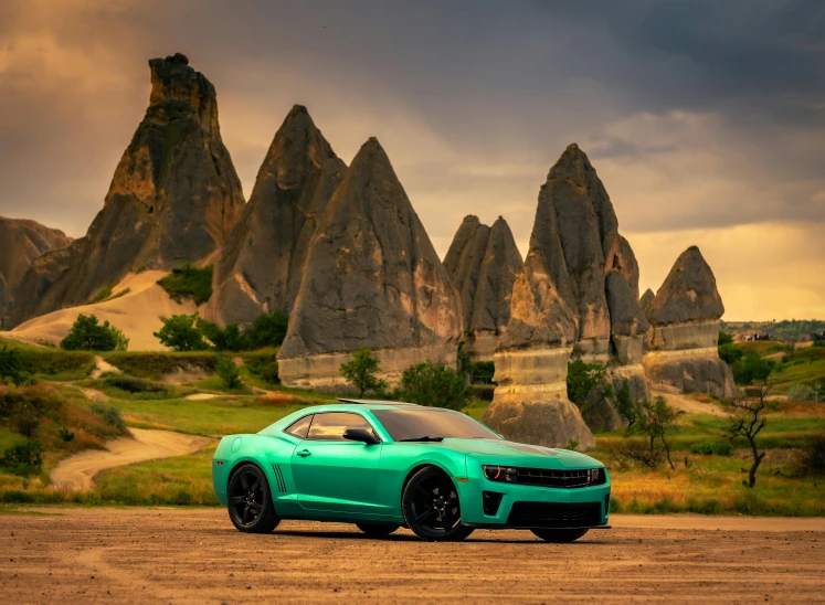 green car driving on dirt road next to mountains