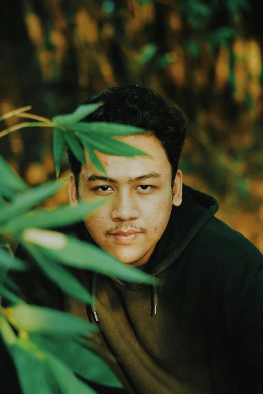 a young man leaning on a plant in the forest