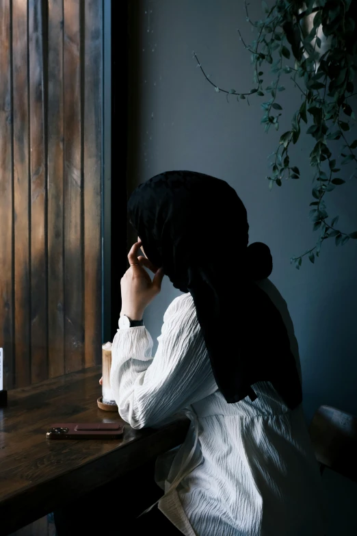 a woman in a black hat sitting at a wooden table talking on the phone