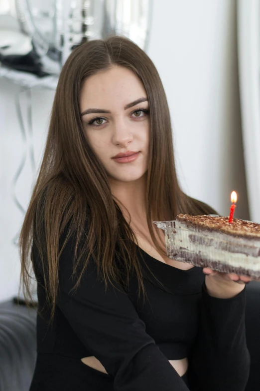 a woman holding up a piece of cake with a lit candle