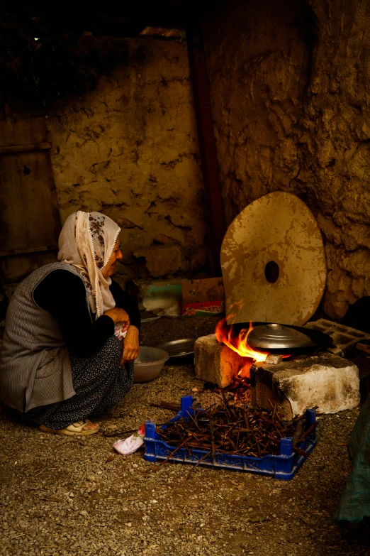 a woman sitting next to a fire in a stone walled area