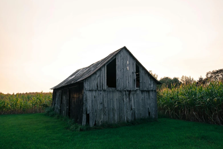 a wooden barn sitting in the middle of a green field