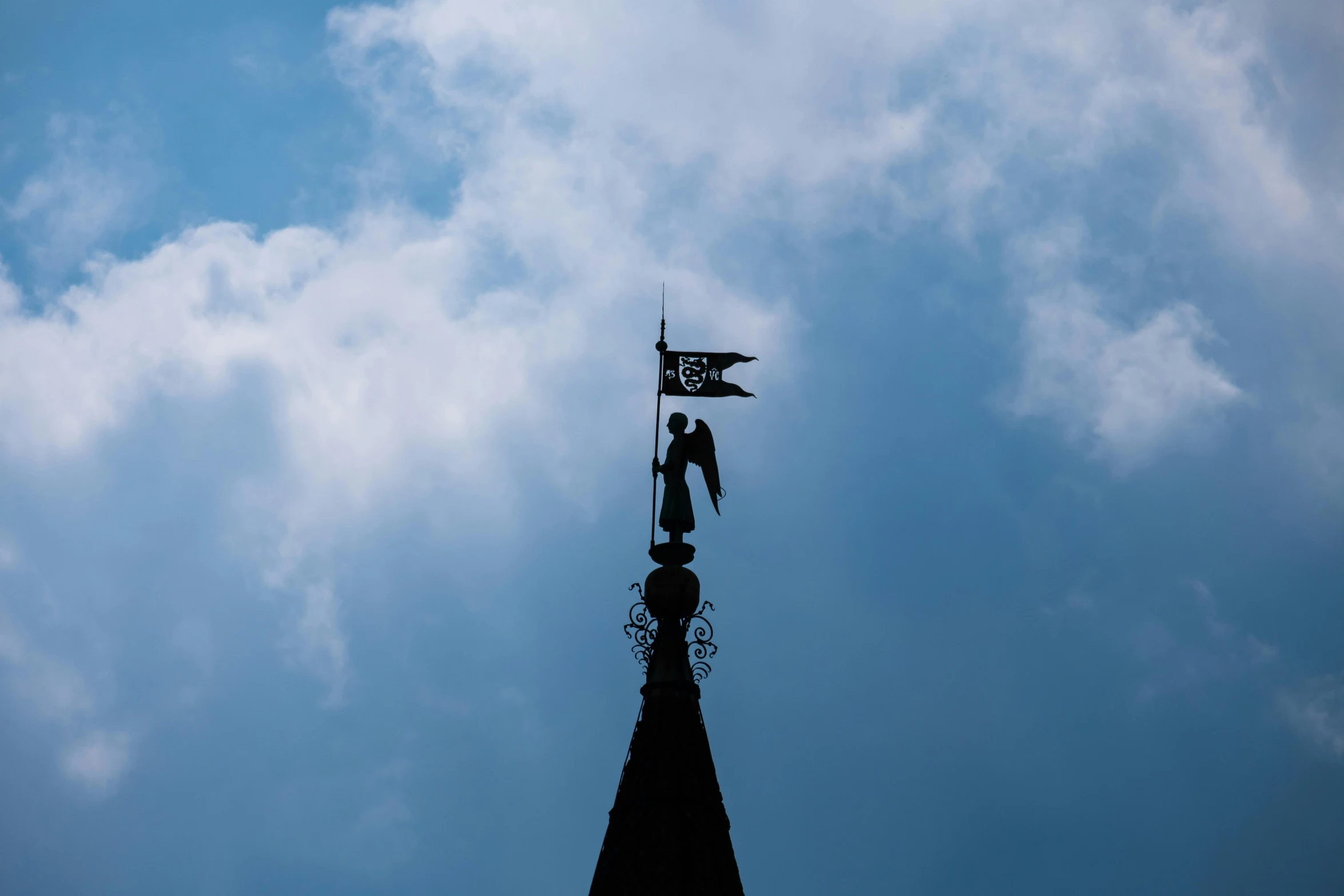 a clock tower with a flag on top and clouds behind