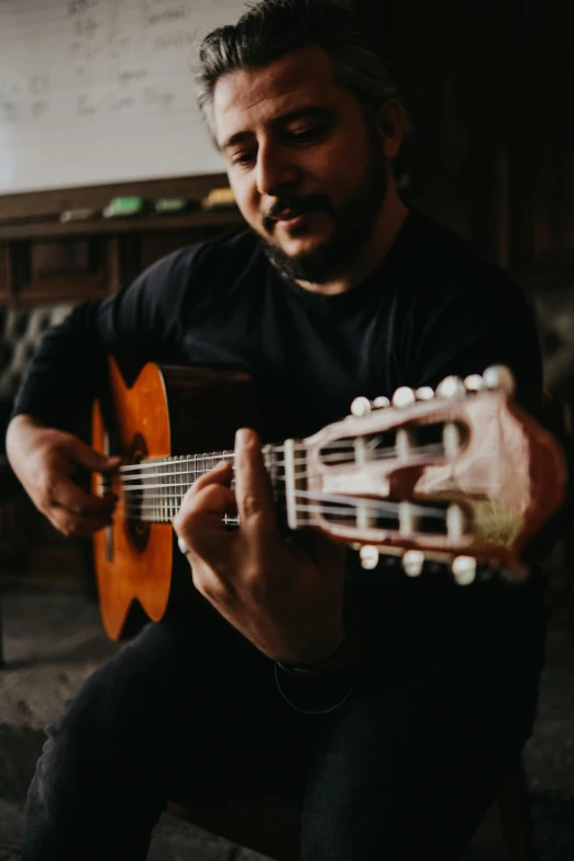 a man with a beard sitting and playing a guitar