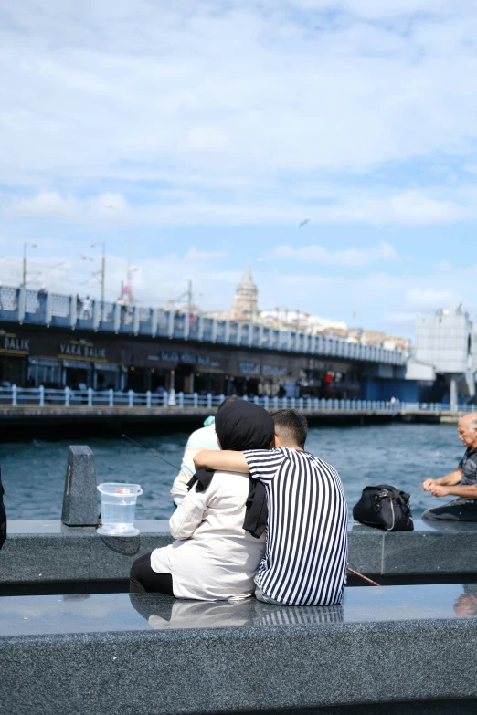 two people sitting on a ledge facing the water