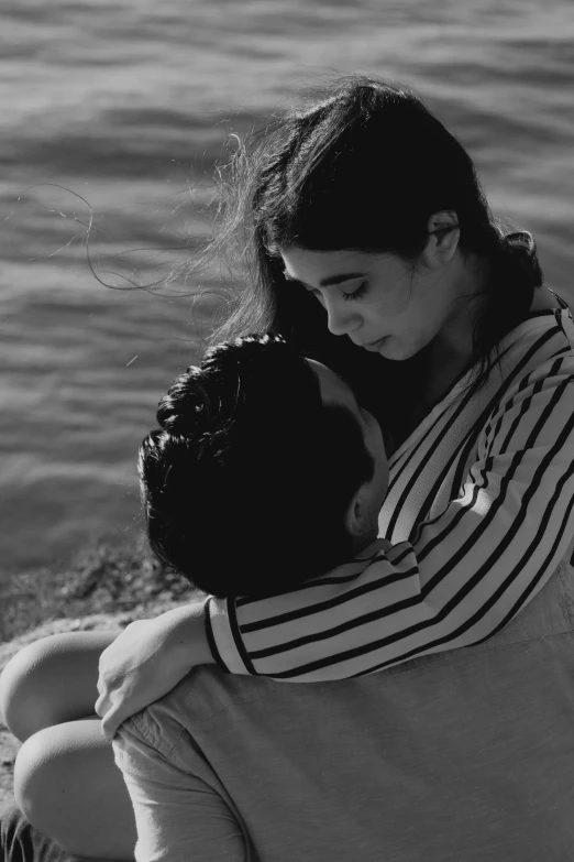 a young woman cuddles her younger son by the water